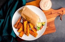 Roasted Vegetable and Halloumi Wrap Served with Sweet Potato Wedges: Vegetarian wrap with zucchini, red bell peppers, arugula, mushrooms, onions, harissa, and halloumi cheese