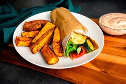 Roasted Vegetable and Halloumi Wrap Served with Sweet Potato Wedges: Vegetarian wrap with zucchini, red bell peppers, arugula, mushrooms, onions, harissa, and halloumi cheese
