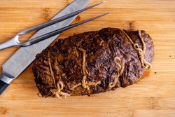 Whole Stuffed Flank Steak with Prosciutto and Mushrooms Overhead: Unsliced steak roulade on a cutting board with a carving knife and fork