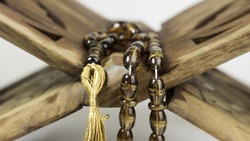 Tasbih, scripture, rosary or prayer beads on wooden bookstand for the Koran. Slightly defocused and close-up shot.