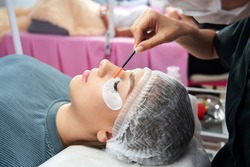 Cosmetologist making eyelash extention and correction using brush