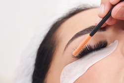 Cosmetologist making eyelash extention and correction using brush