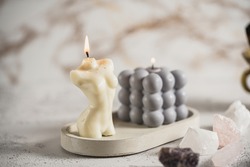 A grey bubble candle and a white candle shaped as a female body on a concrete tray