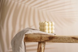 An off-white square bubble candle on a linen cloth on a rustic wooden table in a tropical setting