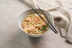 Deep grey japanese style bowl with pasta spaghetti with heavy cream and roasted shrimps with garlic sauce and parmesan cheese, black chopsticks on grey concrete surface