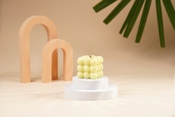 Pale green bubble candle burning on two white round podiums in peach colored arched doors for cosmetics photography on beige colored background