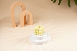 Pale green bubble candle burning on two white round podiums in peach colored arched doors for cosmetics photography on beige colored background