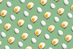 hard light pattern of a fried egg with unbroken egg yolk and a whole raw or boiled egg in egg shell on a seamless green background