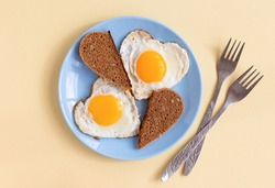 top view of two heart-shaped scrambled eggs with toasts, a pair of fried eggs on blue plate on beige background, romantic minimalistic design, healthy breakfast for sweetheart