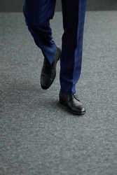 A man in shoes walks forward on the gray floor,close-up.A man is walking along a narrow corridor,only his feet are visible.Successful businessman goes to a business meeting.Business,management concept
