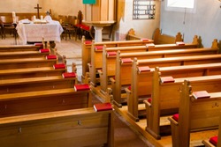 Empty wooden church benches of a Christian church with bible or choir books with cross . Blurry alter in the background. Selective focus. Concept of church service or empty churches.