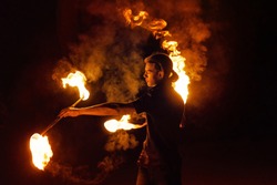 Fire show. Fire dancer dances with two Staff. Night performance. Dramatic portrait. Fire and smoke. A fascinating movement of the flame.