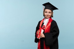 Whizz kid 9-11 year girl wearing graduation cap and ceremony robe with certificate diploma on light blue background. Graduate celebrating graduation. Education Concept. Successful elementary school