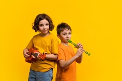 Musical duet in studio on yellow background. Child girl plays ukulele. School boy plays block flute. Two school children practice playing musical instruments