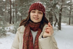 Woman in warm outerwear showing love gesture with fingers in winter forest and looking at camera 