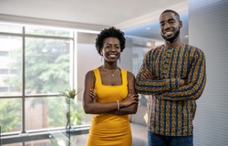Portrait of a two smiling young African businesspeople standing confidently with their arms crossed in a modern office