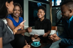 Young African businesspeople laughing together while going over paperwork during a casual meeting in an office