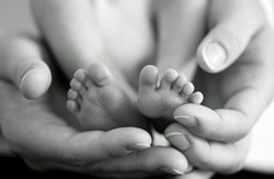 Mother gently hold baby leg in hand. Black and white image with soft focus on babie's foot