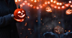 Jack o lantern glowing with moonlight in night forest. Halloween bokeh background with burning orange pumpkin that a men holds in his hands. Happy Halloween banner. Copy space for text