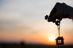 Silhouette of a house figure with a key, a pen with a keychain on the background of the sunset. They dream of a house, moving to a new house, mortgages, renting and buying real estate. Copy space