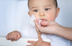 Mom wipes the baby's drool with a napkin. Baby care, teething, drooling.