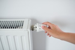 Woman Hand Adjusting The Knob Of Heating Radiator. The valve from the radiator - Heating. Hand adjusting thermostat valve of heating radiator in a room. Copy space.