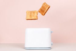 Toasts jumping out of white toaster. Levitation food. Delicious breakfast concept. Pink background. Copy space. Flat lay, side view. Kitchen equipment for fresh morning meal.