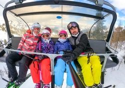 Family riding ski lift cable car on winter vacation skiing. Family on winter vacations ski trip taking selfie on ski lift with amazing mountain view of the ski resort and slopes. Active Family