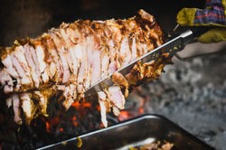 Hand cutting home made cag kebab gyros with a knife - fire and charcoal. is pieces of meat on a big skewer, grilled in a BBQ fireplace and cut with a knife when needed.