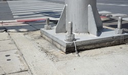 A large screw and hexagon flange nut at the base of the pillar, which is on the pavement. The curb has traffic signs, white and red stripes. On the asphalt road, there are crosswalk.