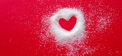 Heart shape on red cloth. Around the heart is white sugar, quite thick, and it fades away with a distance. The appearance of the sugar on the outside looks swaying.