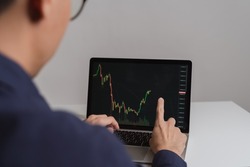Young business trader or investor man is pointing stock market chart ticker, Cryptocurrency graph as Bitcoin graphs on device as computer laptop, smartphone at home. Young money investing concepts.