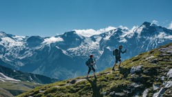 Two young hikers (a couple) walking up a mountain in Austria in summer, with scenic snow covered mountains on the background