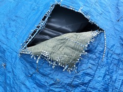 Blue tarp tarpaulin being used to cover a rubbish skip with a torn patch