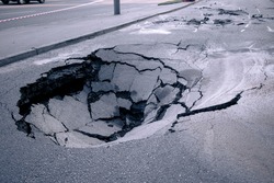 A hole in the ground in the middle of the road. A large pit in the asphalt due to a pipeline accident