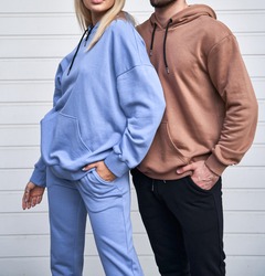 Blonde girl is standing in blue sport outfit. Man wears brown hoodie and black pants. Couple is wearing street matching outfit