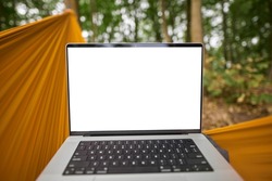 POV of working with a laptop remotely in the woods while hanging in a hammock. Modern laptop empty screen mockup. Design template of a notebook in the forest.
