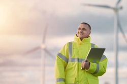 Wind turbine engineer. Male engineer maintains and controls wind turbine energy generation on the background of windmills. Concept of sustainable future.