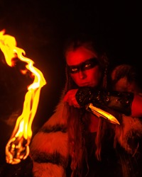 Blonde girl in the image of a Viking in animal skin, with a knife and a burning torch in a dark cave.