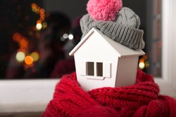 house in winter - heating system concept and cold snowy weather with model of a house wearing a knitted cap