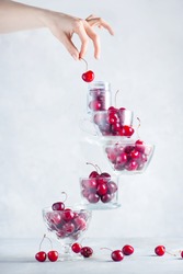 Cherry on top of a balancing stack of bowls and cups filled with berries. Final touch concept on a white background with copy space