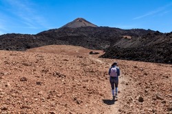 Woman with backpack on volcanic desert terrain hiking trail leading to summit volcano Pico del Teide, Mount Teide National Park, Tenerife, Canary Islands, Spain, Europe. Solidified lava, ash, pumice