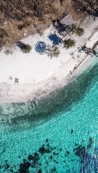 A drone shot of couple lying on a beach on a paradise island in Komodo National Park, Flores, Indonesia. Brownish island turns into white sand beach and further into green and navy sea. Honeymooners