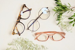 several trendy stylish glasses and flowers on a beige background place copy top view, optics, shop of glasses and frames concept