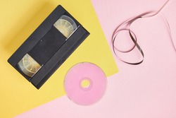cd disc and videotape on pink and yellow background, vintage video cassette and compact disc with pink label copy space top view