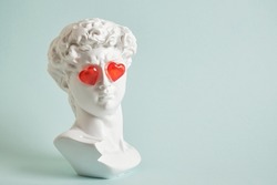 fake bust of david with red glass hearts on the eyes, love concept, valentine's day congratulations copy space light blue background