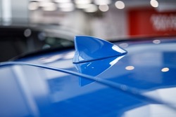 Close-up GPS antenna shark fin shape on a roof of car for radio navigation system. Antenna shark fin on blurry background. Car detail. Classic blue color car. Soft blur background