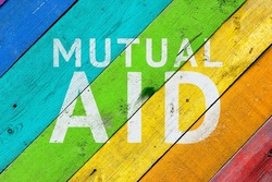 Wooden background in the colors of the flag of the LGBTQ community with the inscription Mutual Aid.