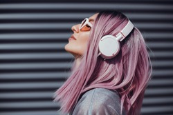 Beautiful young girl with purple pink hair listening to music on headphones, street style, outdoor portrait, hipster girl, music, mp3, Bali, beauty woman, sunglasses, orange color, concept