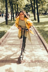 Beautiful young girl in a yellow raincoat riding an electric scooter, hoverboard, in orange sunglasses with long hair, street-style, city, smiles and pleasure, for fan, hipster, driver, emotional